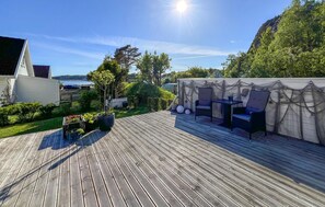 A wooden deck with outdoor furniture, a white building, and a view of a body of water. - Gorgeous home in Lindesnes with WiFi (Lindesnes)
