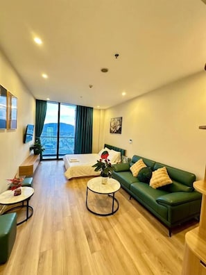 Un hotel moderno con un sofá verde, una mesa de centro redonda, una cama y vistas a la ciudad.