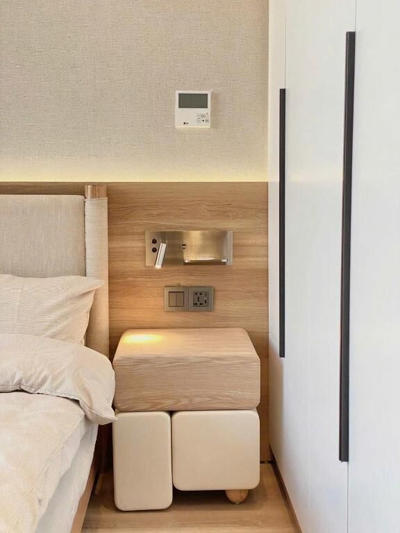 Un dormitorio con cama, mesita de noche y termostato en la pared.