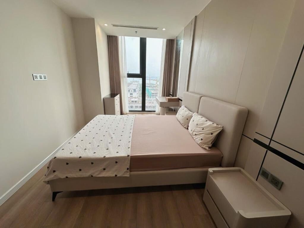 Un dormitorio con cama, mesita de noche, cómoda y ventana con vista a la ciudad.