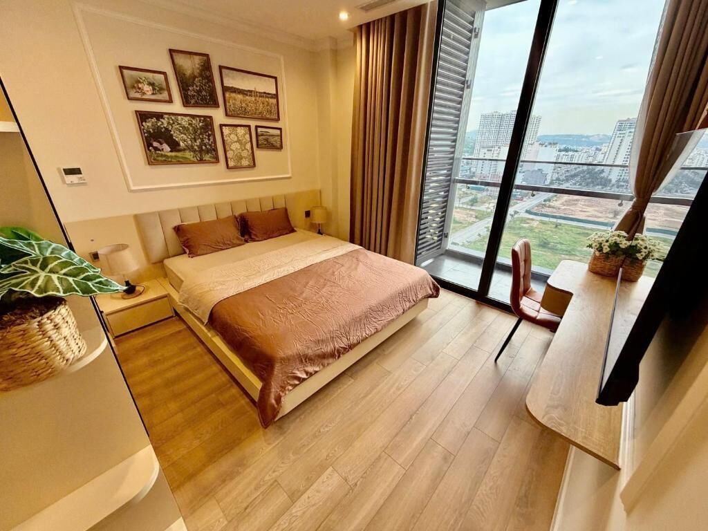 Habitación de hotel con una cama grande, un escritorio, una silla, una ventana con vista a la ciudad y obras de arte en la pared.