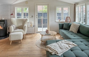 Ein gemütliches Zimmer mit Kamin, einem grünen Sofa, einem flauschigen Sessel und einem kleinen runden Tisch mit Lampe.
