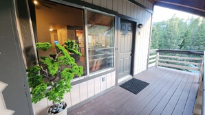 A wooden deck with a potted tree, a sliding glass door, and a view of a residential area.