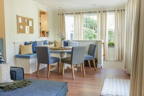Une pièce chaleureuse avec une table à manger en bois, quatre chaises, un banc avec des coussins, un canapé et une fenêtre avec des rideaux.