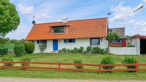 Une maison avec un toit recouvert de tuiles rouges, une porte bleue et une cour clôturée.