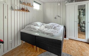 En säng med en svart sänggavel, ett trägolv och en vit vägg med vertikala linjer.