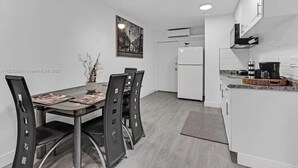 A modern kitchen with white cabinets, a white refrigerator, and a dining area with a glass table and black chairs. - Cozy 1-bedroom house in pleasant Pompano Beach with AC (Pompano Beach)