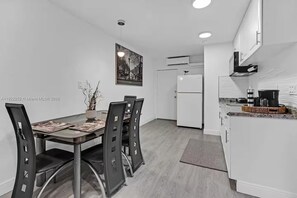 A modern kitchen with white cabinets, a white refrigerator, and a dining area with a glass table and black chairs. - Cozy 1-bedroom house in pleasant Pompano Beach with AC (Pompano Beach)
