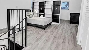 A bedroom with a bed, built-in shelving, a desk, and a staircase. - Cozy 1-bedroom house in pleasant Pompano Beach with AC (Pompano Beach)