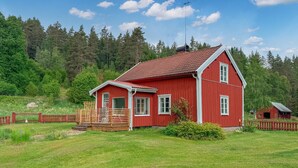 Et rødt træhus med skråt tag, veranda og en indhegnet have.