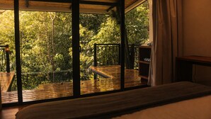 A room with a large window, a wooden deck, and a view of a forest.