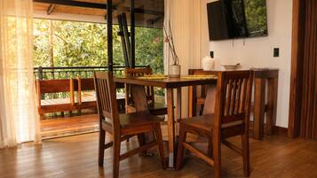 Un tavolo da pranzo in legno con sedie, una televisione montata a parete e un balcone con ringhiera.