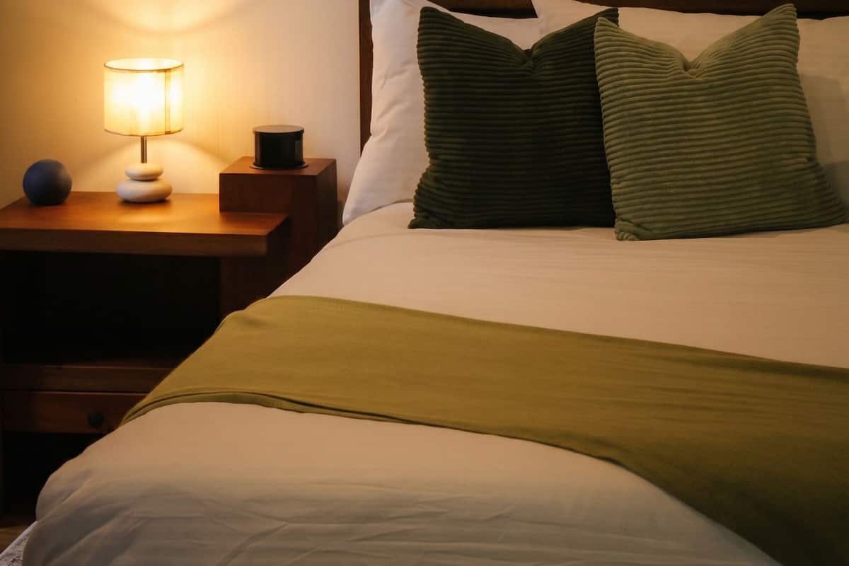 A neatly made bed with pillows and a bedside lamp on a wooden nightstand.