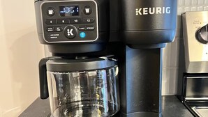 Een Keurig koffiezetapparaat met een glazen kan en een koffiepot op een aanrecht.