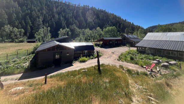 A rural property with multiple buildings, including a barn and cabins, surrounded by a forested hillside. - Durango Oasis: Trout Ponds, Wildlife & Trails (Durango)