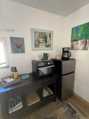A compact kitchenette with a microwave, coffee maker, and refrigerator. There are wall art pieces and a small window. - Durango Oasis: Trout Ponds, Wildlife & Trails (Durango)
