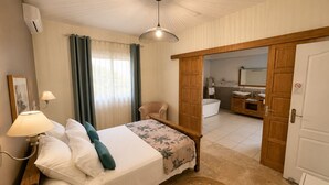 Ein Schlafzimmer mit Bett, Nachttischlampe und Blick ins Badezimmer.