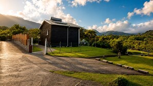 A building with a sloped roof, surrounded by a fenced area with a grassy lawn and trees. - Petit Eden du Bras Piton (Chalet) (La Plaine-des-Palmistes)