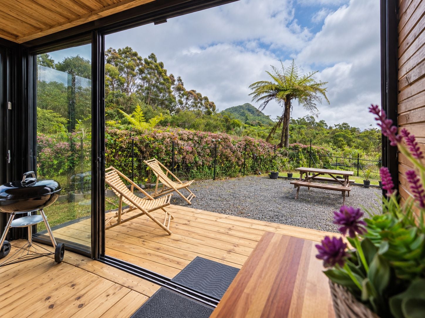 A wooden deck with a grill, two lounge chairs, and a picnic table.