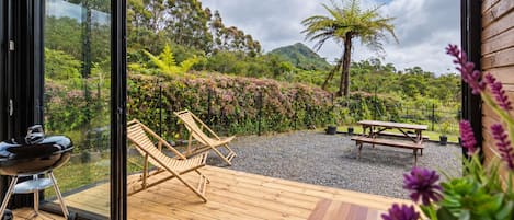 A wooden deck with a grill, two lounge chairs, and a picnic table.