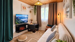 A cozy living room with a fireplace, a sofa, a TV, and a hanging light fixture. - Petit Eden du Bras Piton (Chalet) (La Plaine-des-Palmistes)
