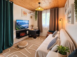 Un salon chaleureux avec une cheminée, un canapé, un téléviseur et un luminaire suspendu.