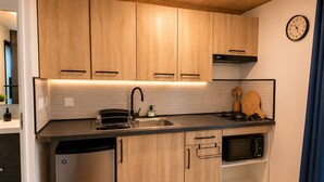 A compact kitchen with wooden cabinets, a stainless steel dishwasher, a microwave, and a gas stove. - Petit Eden du Bras Piton (Chalet) (La Plaine-des-Palmistes)