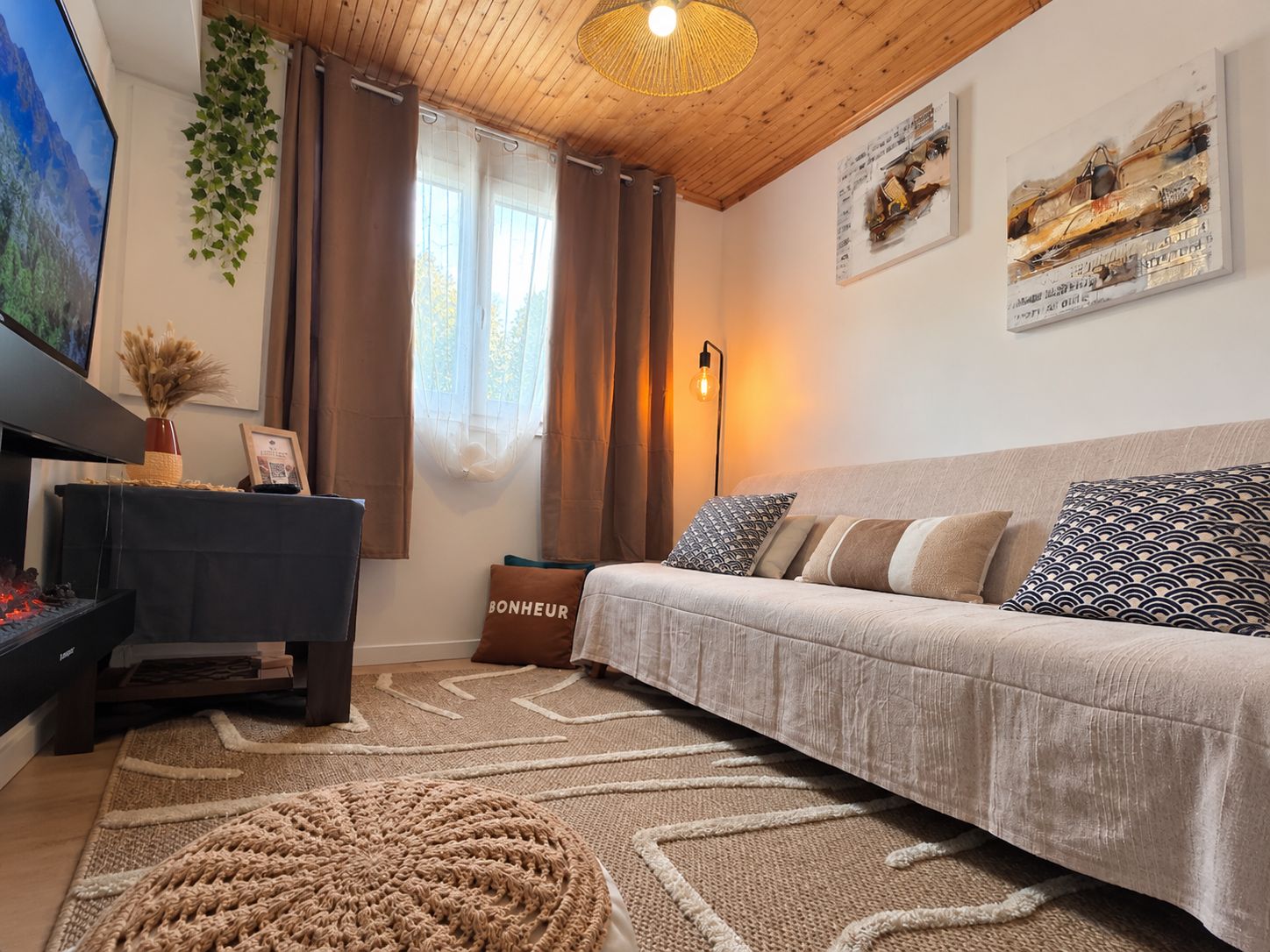 Ein gemütliches Wohnzimmer mit einer Couch, einem Fernseher, einem Kamin und dekorativen Kissen.