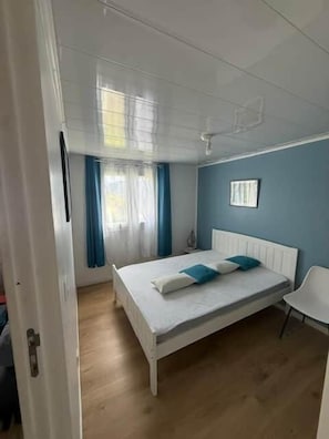 Een slaapkamer met een bed, een stoel, een raam met gordijnen en een radiator.