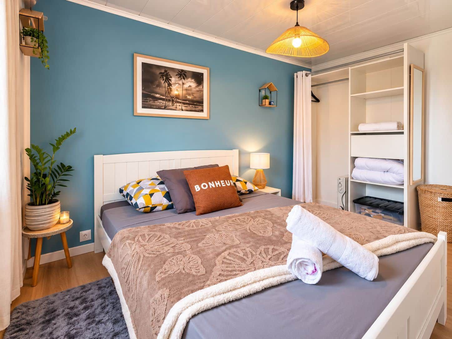 Ein Schlafzimmer mit Bett, Nachttisch, Lampe, Topfpflanze, gerahmtem Bild und Kleiderschrank.