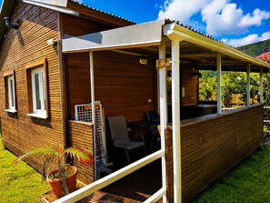 Une cabane en bois dotée d’un patio couvert, d’une petite table, de chaises et d’une plante en pot.