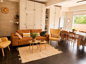 Ein Wohnzimmer mit einer Couch, Sesseln, einem Couchtisch und einem Essbereich mit Tisch und Stühlen.
