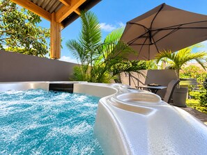 A hot tub with a wooden pergola overhead, surrounded by lush greenery and a clear blue sky. - L'Eden de Bois Noir (villa 2 avec jacuzzi) (Saint Joseph)