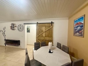 Un comedor con una mesa redonda, sillas, una chimenea, una puerta de madera y un reloj de pared.