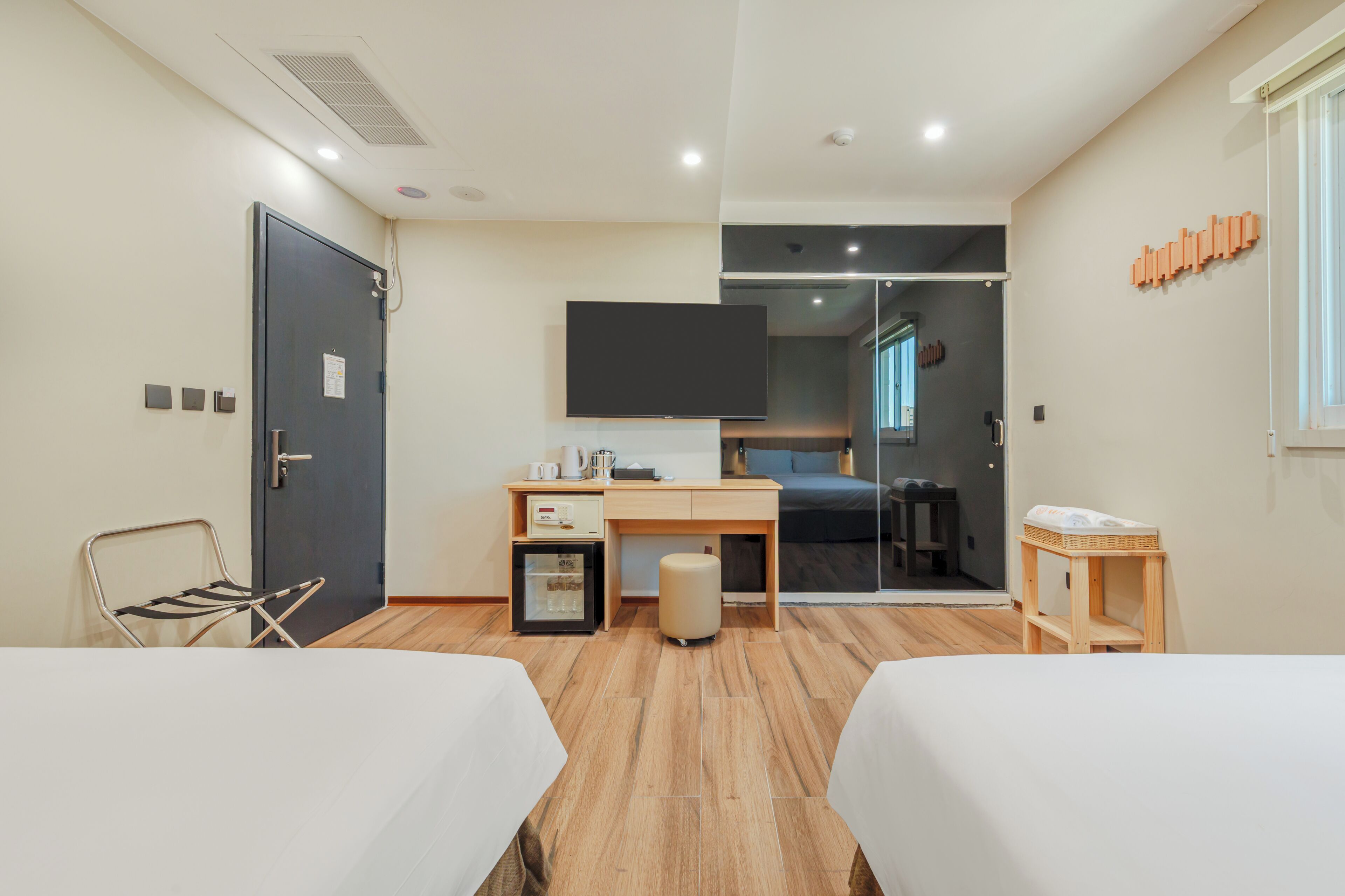 Habitación de hotel con dos camas, un escritorio, televisión, un refrigerador pequeño y una ventana.