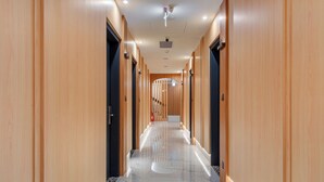 A modern hotel corridor with wooden paneling, marble flooring, and ceiling-mounted security cameras. - WHIYORI INN (Kaohsiung)