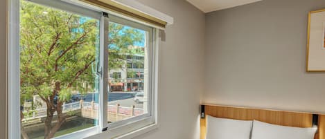 Habitación de hotel con un ventanal grande, una cama con ropa blanca y vistas a la calle y a los árboles.