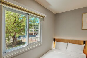 A hotel room with a large window, a bed with white linens, and a view of the street and trees outside. - WHIYORI INN (Kaohsiung)