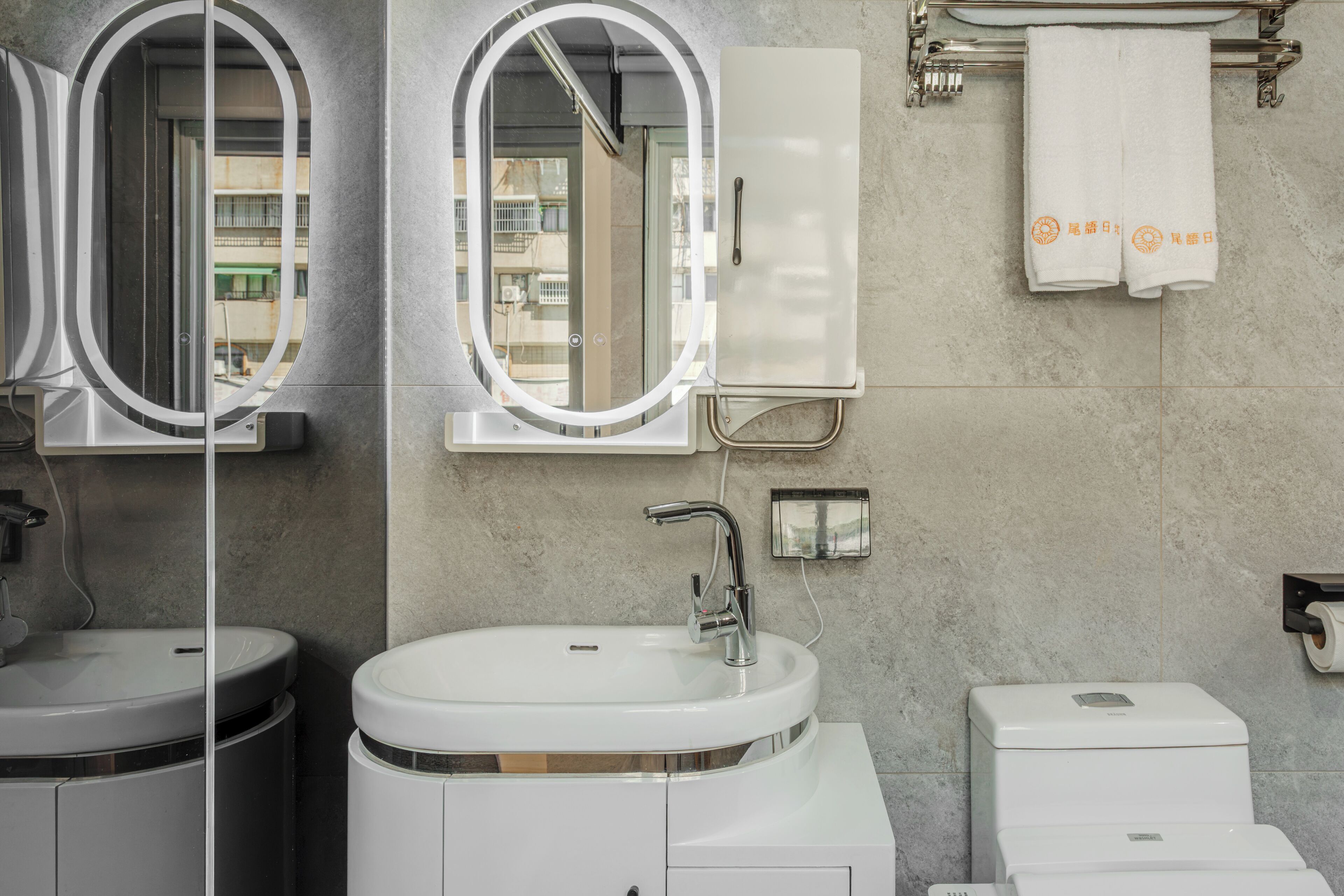 Un baño moderno con un lavamanos blanco, un espejo, un perchero para toallas y un inodoro.