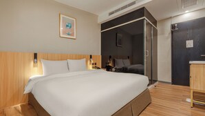 A hotel room with a large bed, a bedside table, a nightstand, a wall-mounted phone, and a door leading to a bathroom. - WHIYORI INN (Kaohsiung)