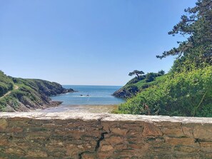 Eine Küstenlandschaft mit einer Steinmauer, einem schmalen Pfad und freiem Blick auf das Meer.
