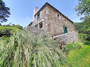 Ein Gebäude aus Stein mit steilem Dach, Schornstein und grüner Tür.