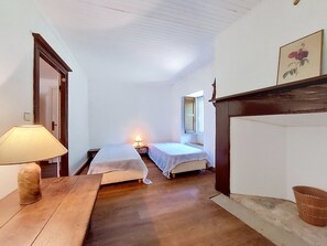 A room with two beds, a wooden table, a lamp, a window, and a painting on the wall. - La Sardinerie de la Crique de Porsac'h by Interhome (Le Pouldu)