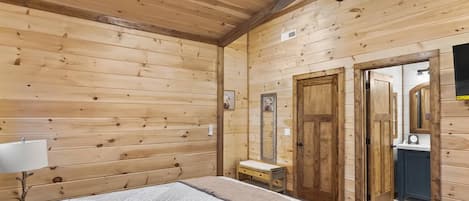 A wooden cabin room with a bed, a small bedside table, a ceiling fan, and a mirror.