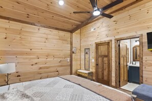 Een houten kamer met een bed, een klein nachtkastje, een plafondventilator en een spiegel.