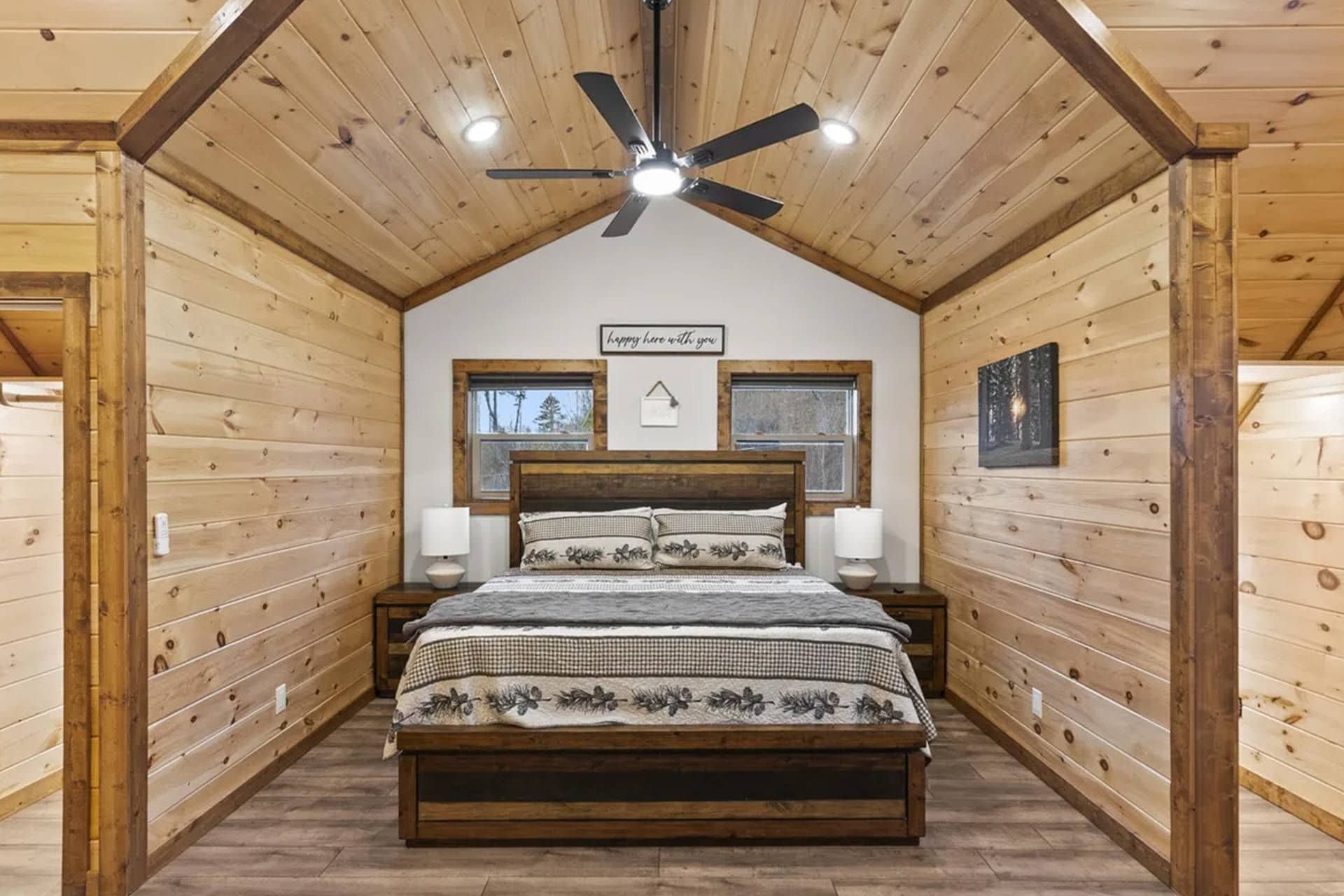 A wooden cabin bedroom with a bed, two bedside tables, a ceiling fan, and a window.
