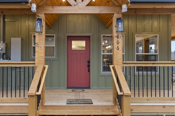 A wooden cabin with a red door, a number '406' on the wall, and a 'welcome' mat at the entrance. - Fall Family Retreat | New Cabin Near Gatlinburg (Sevierville)