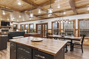 A spacious living area with a fireplace, a sofa, a dining table set for four, and a kitchen island. - Fall Family Retreat | New Cabin Near Gatlinburg (Sevierville)