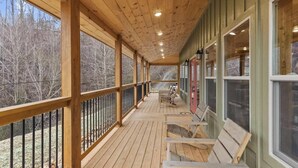 Una terrazza in legno coperta, con panchine, ringhiere e finestre che si affacciano su una zona boschiva.