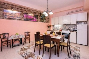A dining area with a brick wall, a chandelier, and a tiled backsplash in the kitchen. - Corfu City Apartments - Kontessa (Corfu, Kerkira)